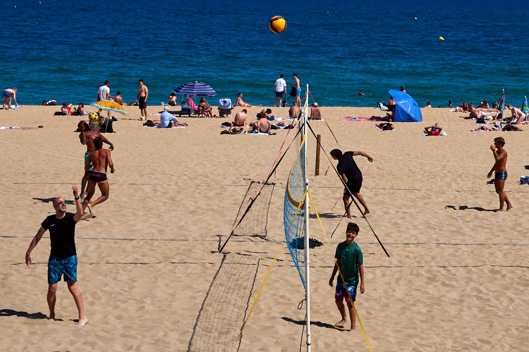 Beach volleyball players beneath a ball suspended over the court